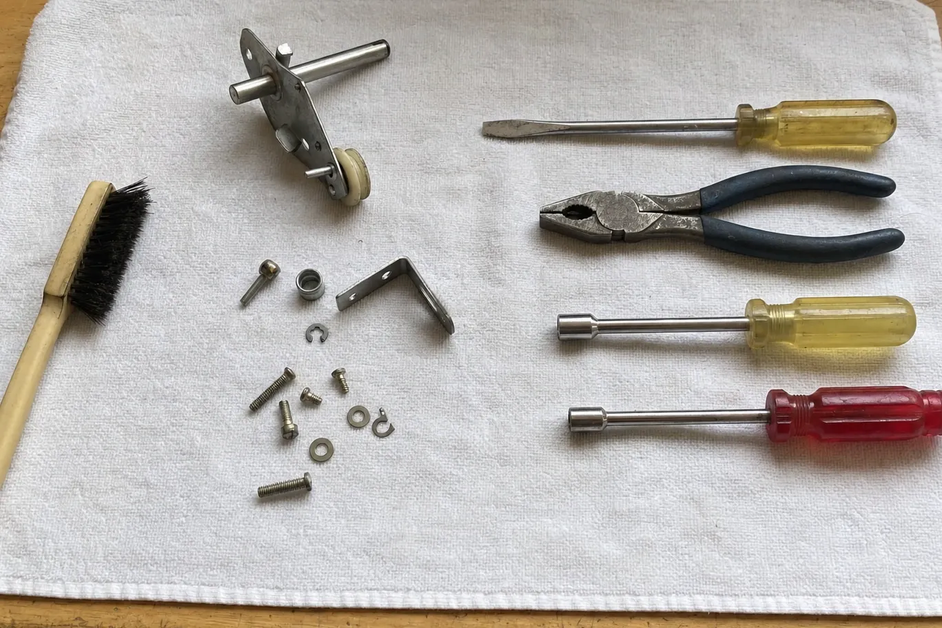 A roller-and-rail assembly with its wheel, small hardware, a brush and four hand tools on a white towel